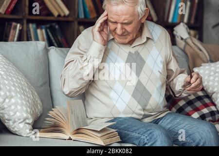 Senior man alone sitting at library reading book having headache Stock Photo