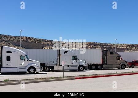 Three big rigs semi trucks of different brands models are lined up in parking lots truck stops or  rest areas filling vacant places to rest have lunch Stock Photo