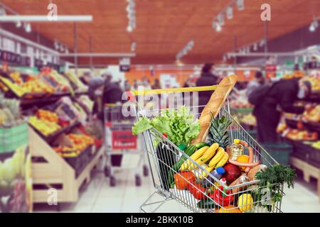 Shopping cart in a supermarket filled with products with customers in protective face masks to protect during the pandemic, Covid 19, or a new coronav Stock Photo