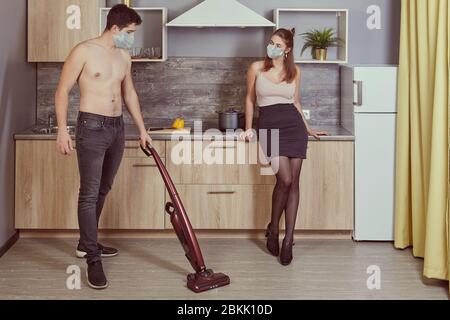 A young family is cleaning kitchen in their home during quarantine in connection with the Covid-19 pandemic. Young man and woman indoors in face prote Stock Photo