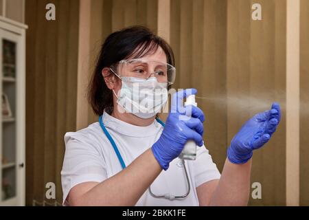 A Healthcare worker sprays antiseptic on surgical gloves on her hands during the covid-19 pandemic. Female doctor uses a sanitizer to disinfect her ha Stock Photo