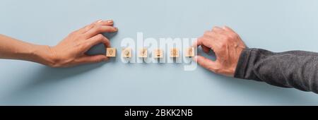Male and female hands placing wooden blocks with contact and communication icons on; them in a row. Wide view image over blue background. Stock Photo