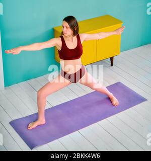 young girl practices yoga in a sports uniform on a purple rug Stock Photo