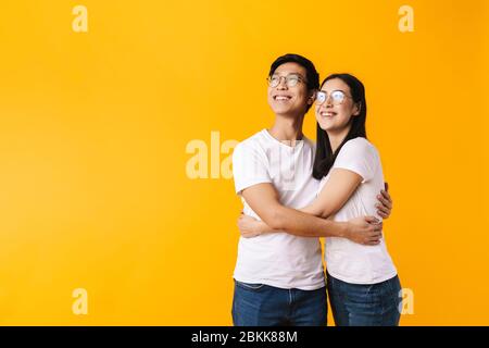 Image of cheerful multinational man and woman hugging and looking upward isolated over yellow background Stock Photo