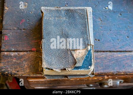 An old, tattered Holy Bible sitting on a wooden bench in an old workshop Stock Photo