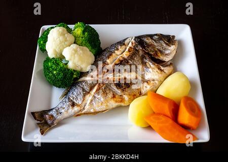 Mediterranean sea dish, Sparus aurata of baked fish vegetables and boiled potatoes on a black background. Healthy food. Stock Photo