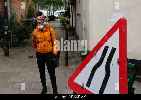 Brixton - London, UK. A teenager, with protective face mask and holding a phone waits at a bus stop during the continuing world covid crisis. Stock Photo