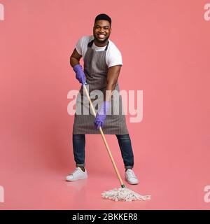 Household Chores. Happy African Janitor Washing Floor With Mop And Smiling Stock Photo