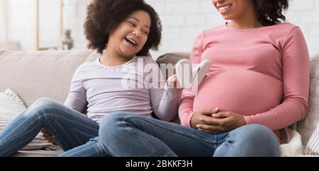 Joyful Little African Girl Playing With Baby Shoes Near Mom's Pregnant Belly
