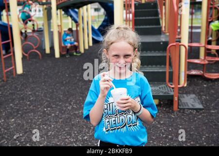 Smiling Curly Haired Girl Eats Slush on School Playground at Field Day Stock Photo