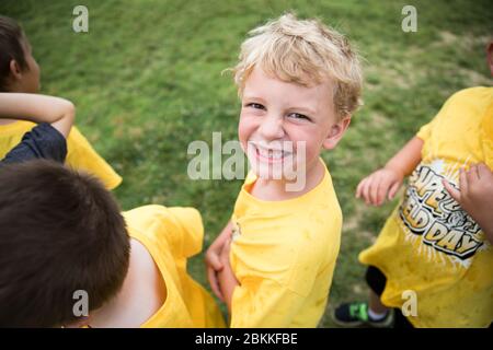 Happy Blonde Boy Smiles at Camera While Standing in Line Outdoors Stock Photo