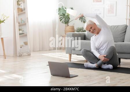 Happy senior woman doing stretching exercises in front of laptop at home Stock Photo