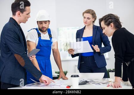 Four young business people working as a team gathered around a chart in an open plan modern office. Stock Photo