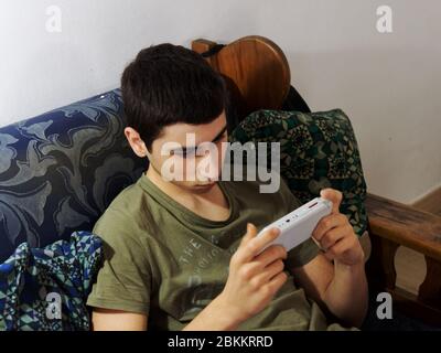 Caucasian boy plays with a portable console on the couch Stock Photo