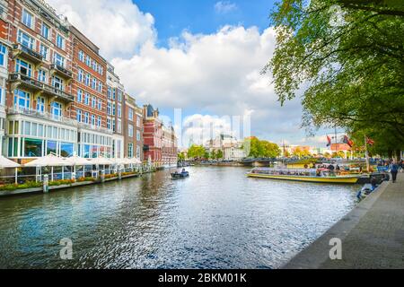 A small boat glides past tourist boats on a large canal near the museum district of Amsterdam in early Autumn. Stock Photo