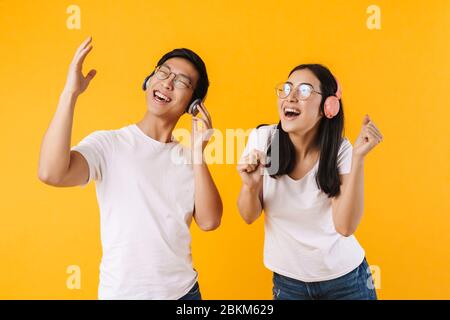 Image of joyful multinational couple in wireless headphones listening music and singing isolated over yellow background Stock Photo