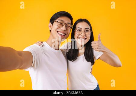Image of joyful multinational couple taking selfie and gesturing peace sign isolated over yellow background Stock Photo