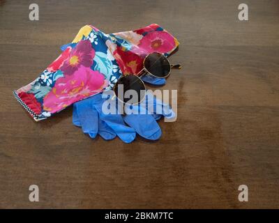 Sunglasses, Handmade Fabric Mask in bright pink floral pattern, and Disposable Blue Gloves on a wooden table. Photographed with a shallow depth of fie Stock Photo