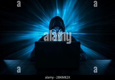 Male thief in gas mask stealing data from computer Stock Photo