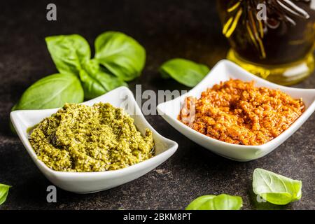Green basil and red tomato pesto dip sauce  and basil leaves on black table. Stock Photo