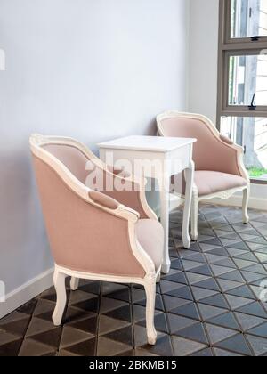 Beautiful classic and vintage sofa set, materials fabric beige color and white wooden and white wooden simple desk on modern stone tiles near glass wi Stock Photo