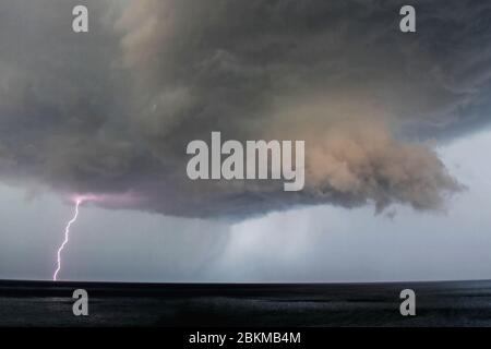 Lightning Bolt coming from Dark Storm Clouds over the sea/ Thunderstorm Clouds with Lightning/ Sea storm Stock Photo