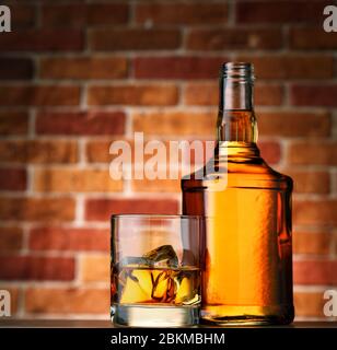 Bottle and glass of whiskey with ice on brick wall background Stock Photo