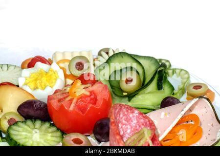 Breakfast on plate with cucumber, tomato, ham, salami, green and purple olives, yellow cheese, boiled egg and red bell pepper Stock Photo
