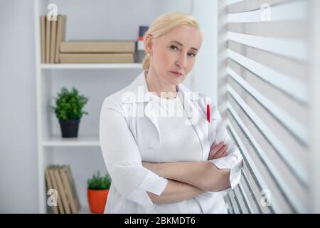 Woman blonde in a white coat clasped hands on her chest. Stock Photo