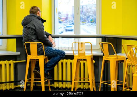 A man sits facing the window, his face is not visible. Yellow cafe interior. lonely man. Stock Photo