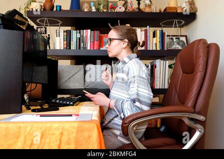 A woman works at home. Look at the computer. Cozy atmosphere, home clothes. Stock Photo