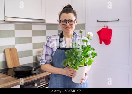 Portrait of housewife woman with potted flower plant at home kitchen Stock Photo