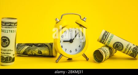 alarm clock both monetary denominations dollars, Time is money. Retro alarm clock and hundred dollar bills on a yellow background Stock Photo