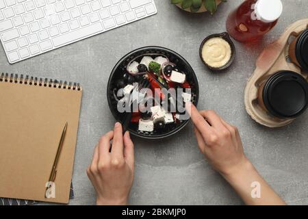 Woman eat salad in takeaway box on gray background. Food delivery Stock Photo