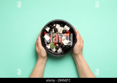 Food delivery. Person holds salad in takeaway box on mint background Stock Photo