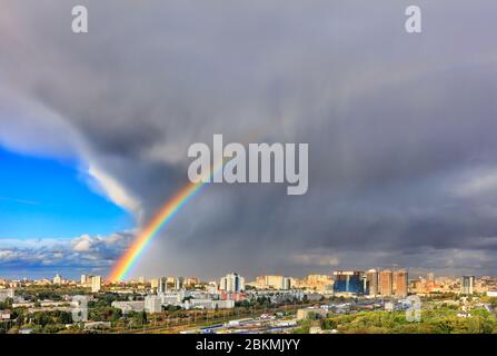 A bright rainbow in the sky above urban houses, sunlight displaces a thunderous front revealing a blue sky. The concept of change for the better. Stock Photo