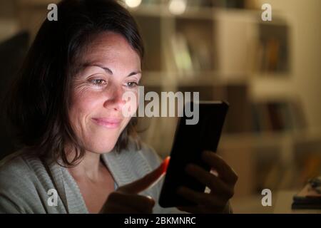 Adult woman using smartphone with lighted screen sitting at night at home Stock Photo