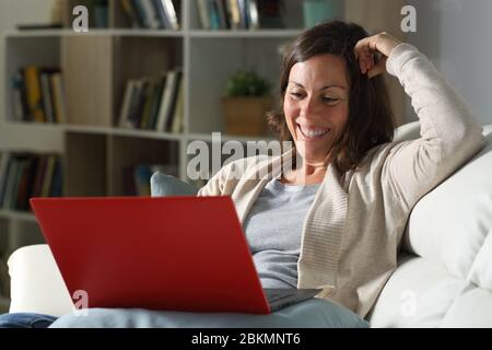 Happy adult woman watching video online on laptop sitting on the sofa at night at home Stock Photo