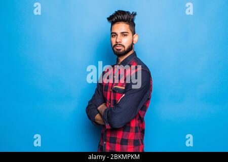 Young indian man wearing casual polo standing over isolated blue background happy face smiling with crossed arms looking at the camera. Positive perso Stock Photo