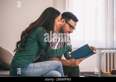 Happy couple is sitting at sofa in their home and relaxing. Stock Photo