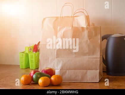 Paper bags, fresh vegetables and fruits next to a mobile phone on the table with kitchen utensils. Concept of shopping, healthy eating and vegetariani Stock Photo