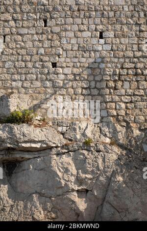 Big bright light coloured limestone rocks with on top of them a limestone brick wall in Dubrovnik, Dalmatia, Croatia on a sunny day. Rustic rough stru Stock Photo