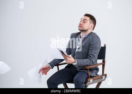 Successful business man businessman in a suit sitting on a wooden chair with a folder of documents and throwing them into the air. On a white backgrou Stock Photo