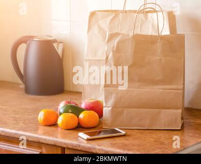 Paper bags, fresh vegetables and fruits next to a mobile phone on the table with kitchen utensils. Online shopping and contactless delivery concept. Stock Photo