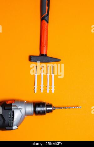 Tools for repair. Hammer for nails, drill, dowel in the wall on an orange background. Toolkit for the wizard Stock Photo