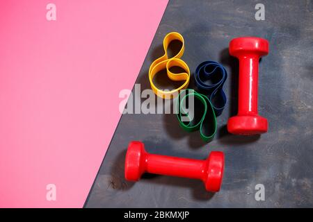 Red dumbbells and elastic bands for sports on a pink background. Healthy lifestyle. Fitness equipment for weight training. Muscle development and fitn