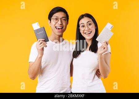 Image of excited multinational couple holding passports with tickets and hugging isolated over yellow background Stock Photo