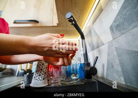 The girl washes her hands under running water in a black washstand. Water faucet, clean dishes, wooden kitchen furniture Stock Photo