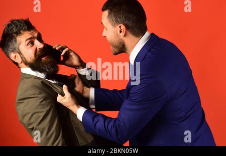 Businessman with surprised face holds mobile phone. Machos in classic suits talk on cell phone. Business talk and rivalry concept. Men with beards fight on red background. Stock Photo
