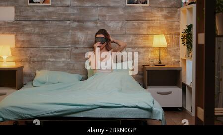 Beautiful woman in pajamas using her phone before going to sleep. Sleep mask. Stock Photo